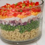 This is an easy and beautiful salad that makes the perfect side dish to bring to a potluck. Layered Pasta Salad has layers of macaroni, red onion, peas, ham, cheese, tomato and is tossed in a ranch dressing.