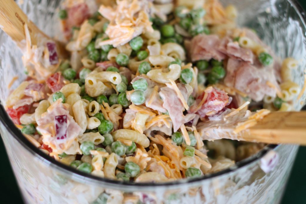 This is an easy and beautiful salad that makes the perfect side dish to bring to a potluck. Layered Pasta Salad has layers of macaroni, red onion, peas, ham, cheese, tomato and is tossed in a ranch dressing. 